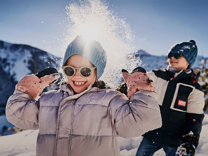 Ein Kind spielt im Schnee während eines Skiurlaubs mit der Familie.