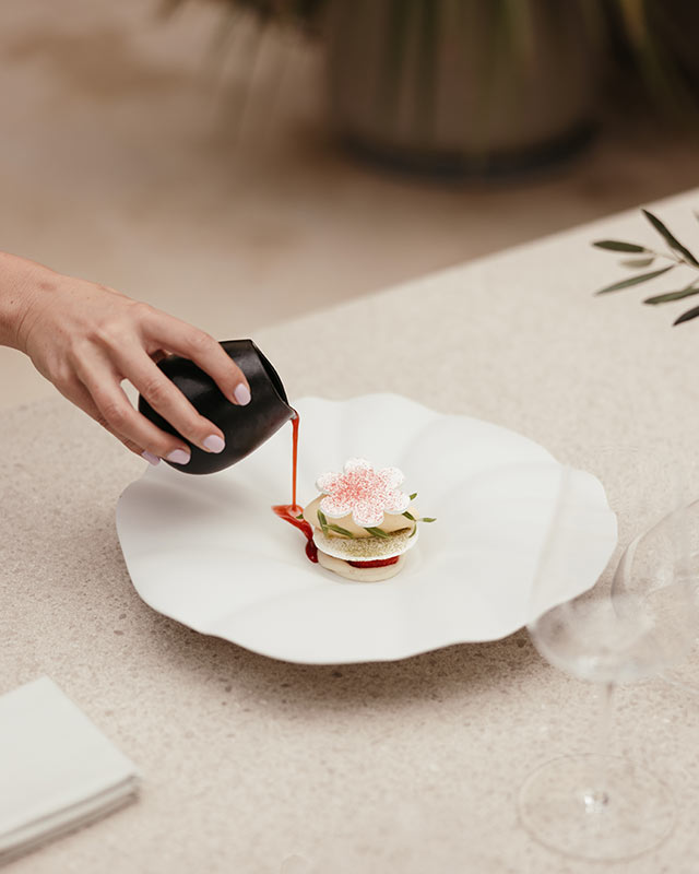 Présentation d’un dessert gastronomique avec une main ajoutant de la sauce à un plat délicatement stylé.