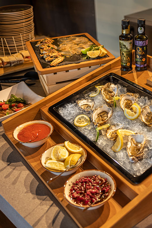 Buffet de fruits de mer avec des huîtres fraîches sur glace, quartiers de citron, sauces et bouteilles d’huile d’olive.