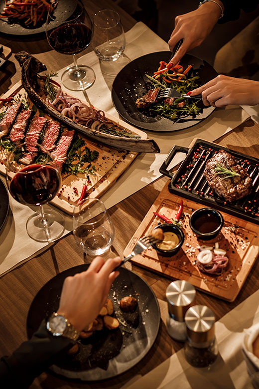 Dîner gourmet avec steaks grillés, légumes rôtis et vin, servis sur des planches en bois élégantes dans un cadre raffiné.