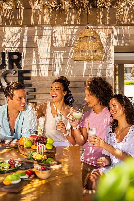 A group of friends laughing and toasting with drinks at a vibrant beachside restaurant