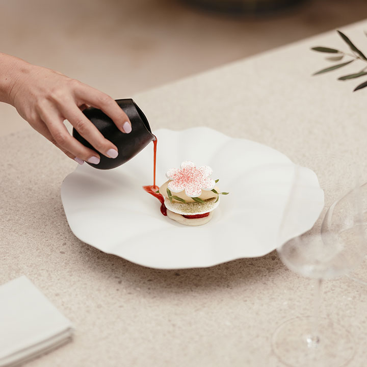 Gourmet-Dessert-Präsentation mit einer Hand, die Sauce auf ein kunstvoll angerichtetes Gericht gibt.