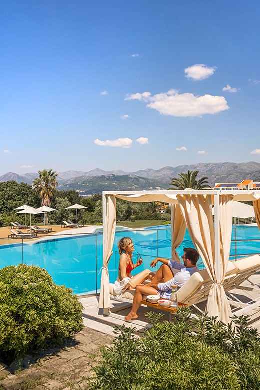 A couple in a setting relaxes on a lounge chair by a pool