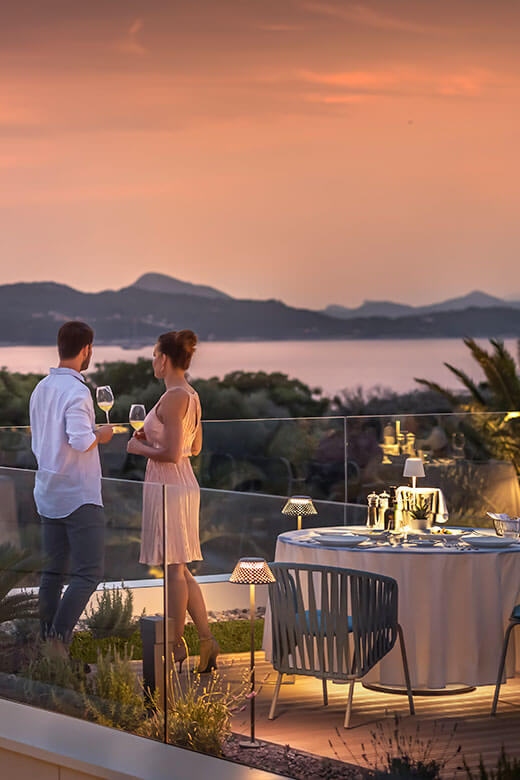 Couple looking at the sunset on a restaurant terrace with wine in hand