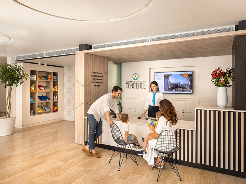 Hotel concierge desk with staff assisting a family, including parents and two children, in a luxury hotel lobby