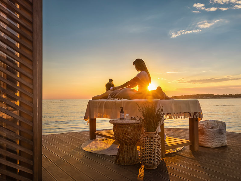 A woman being massaged on a wooden deck at sunset