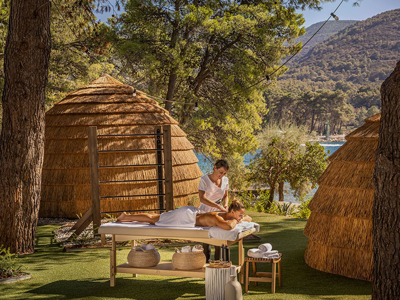 Un terapista esegue un rilassante massaggio all'aperto su un lettino in una spa naturale mediterranea.