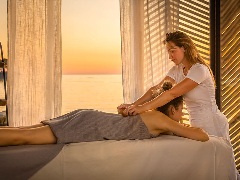 Il terapista della spa esegue un massaggio alla schiena a un ospite con vista sul tramonto sul mare.