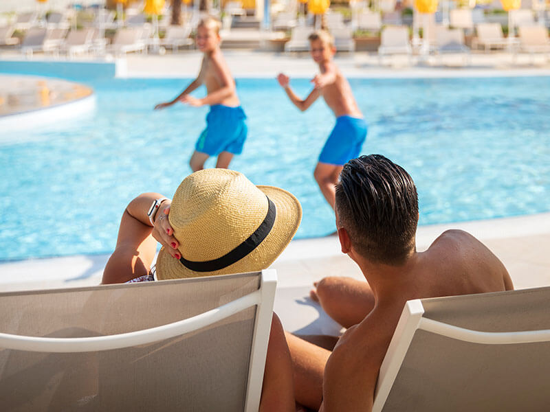 Eltern entspannen am Pool, während ihre Kinder im Wasser spielen