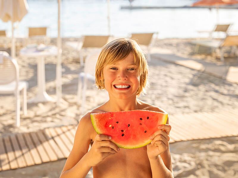 Kind mit einer Wassermelonenscheibe an einem Sandstrand in Istrien