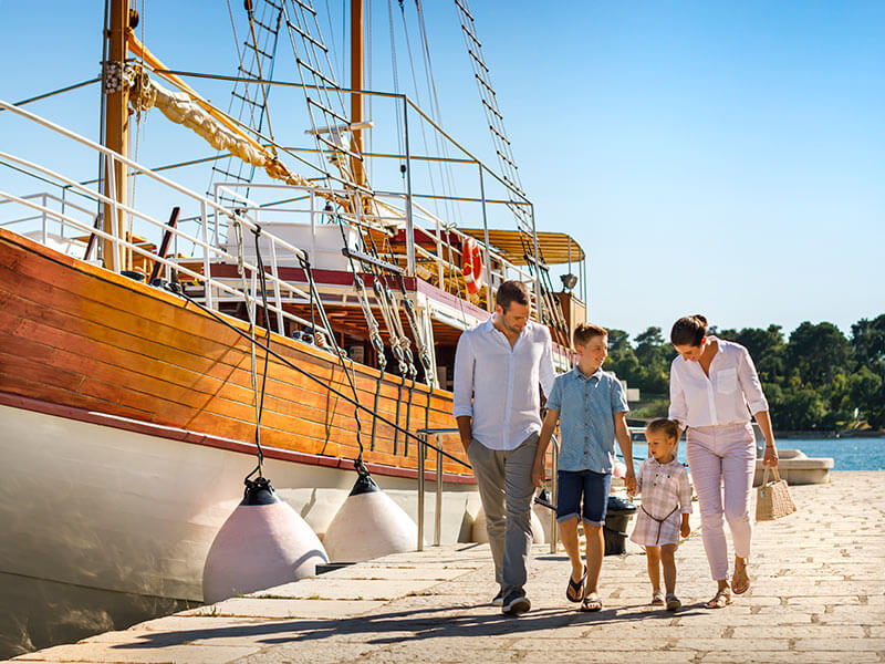 Eine vierköpfige Familie geht neben einem Holzboot einen Pier entlang.